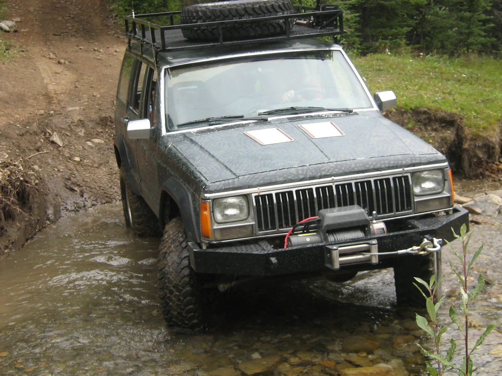 Lifted Jeep Cherokee XJ with roof rack and winch crossing a shallow stream