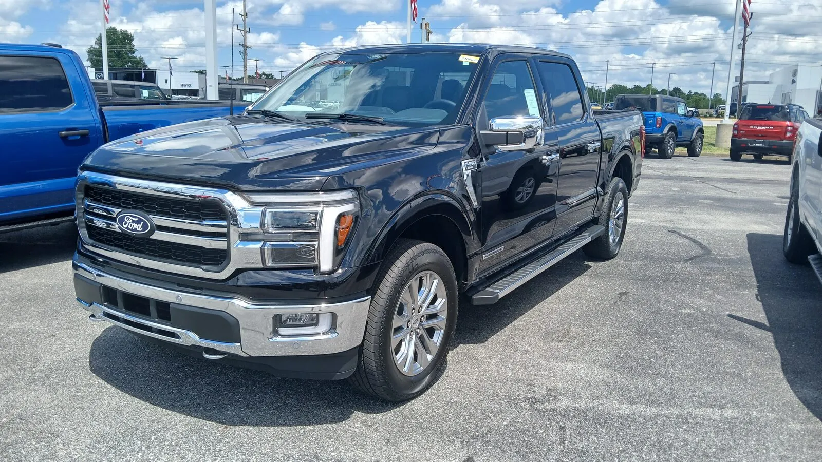Black 2024 Ford F-150 Lariat SuperCrew PowerBoost hybrid pickup, front three-quarter view on a dealer lot