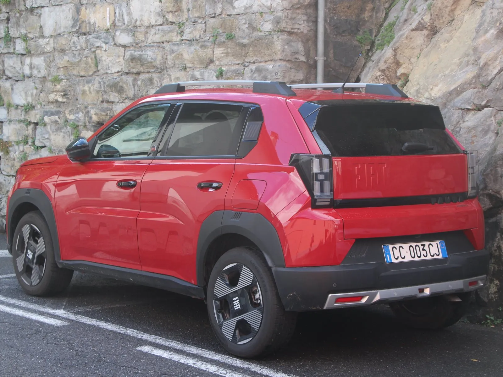 Fiat Grande Panda Hybrid rossa, vista posteriore di tre quarti, parcheggiata accanto a una parete di roccia sul Lago di Como