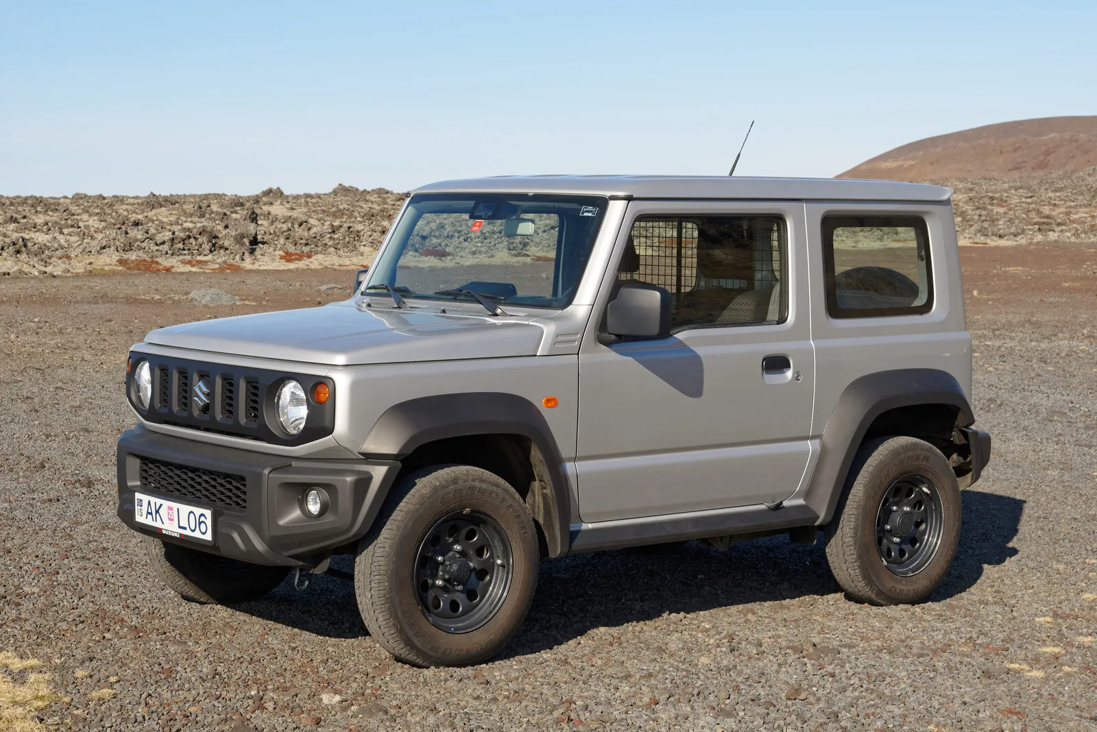 Silver Suzuki Jimny JB74 parked on gravel below a hill in Iceland