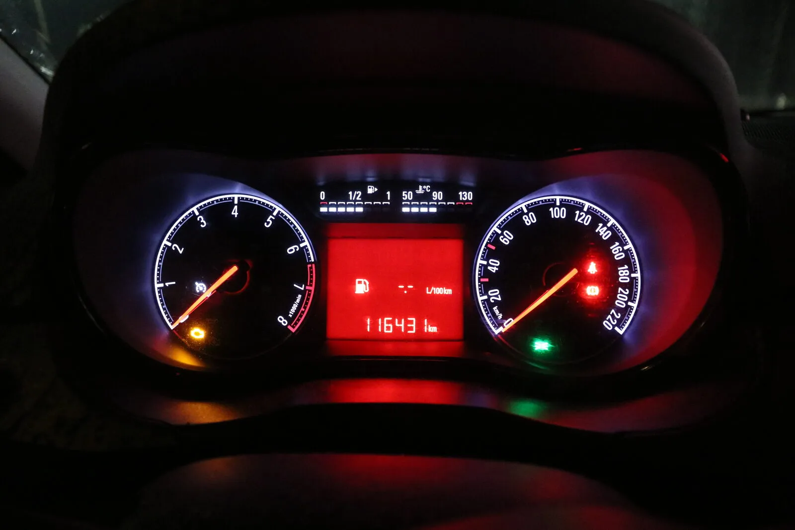 An instrument cluster at night with the digital odometer and the L/100 km consumption display
