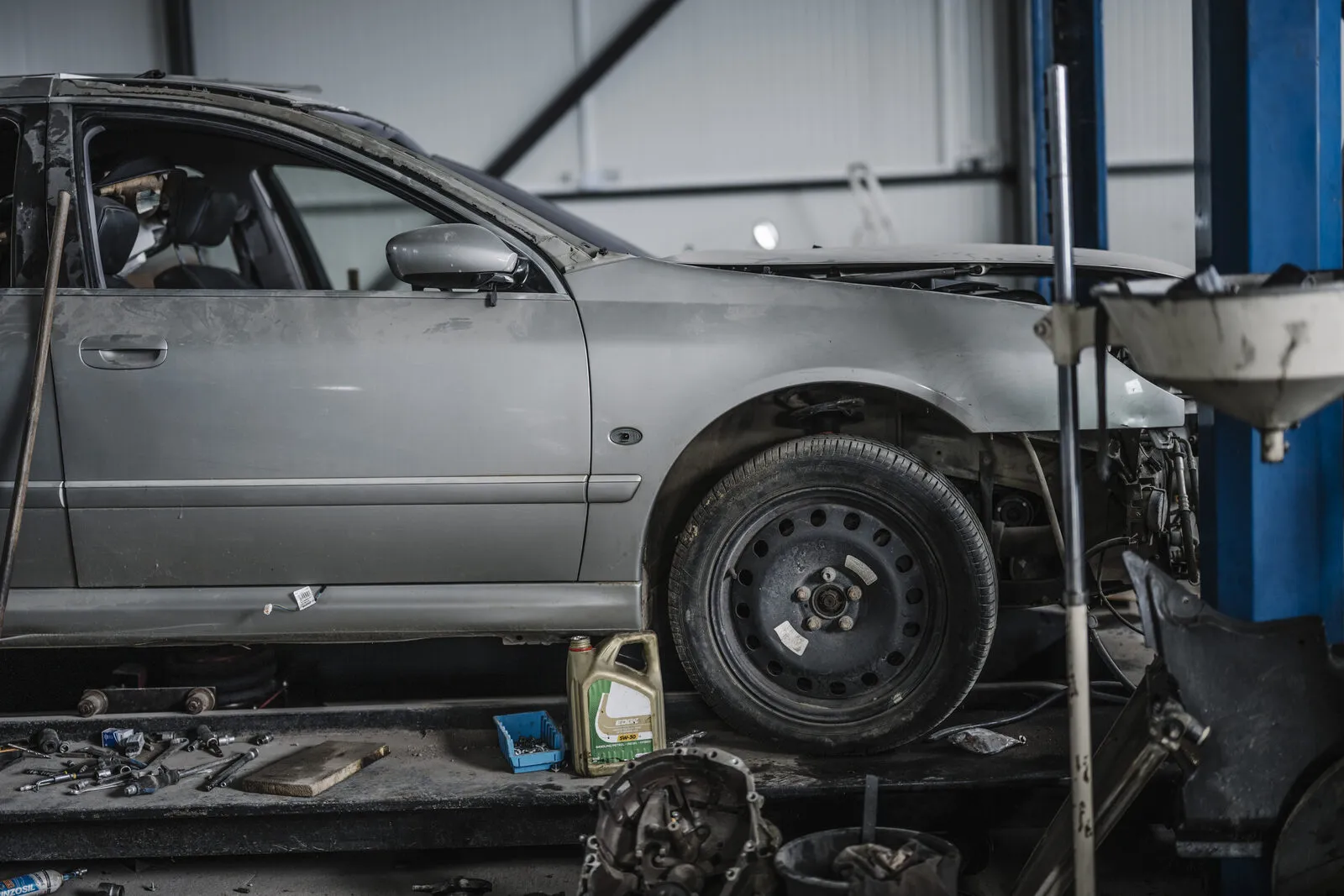 A car on a lift in a repair shop with the front wheel removed and tools on the floor